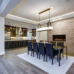 Modern open floor plan dining room design accented with stone fireplace wall facing black dining table lined with leather chairs and illuminated by rectangular chandelier. Northwest, USA